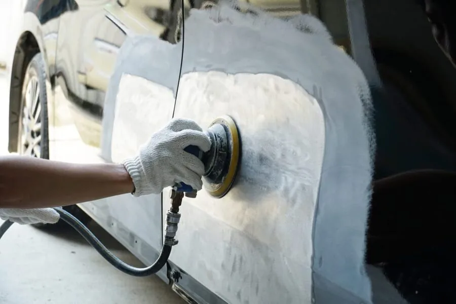 Panel beater sanding a car panel during crash repair