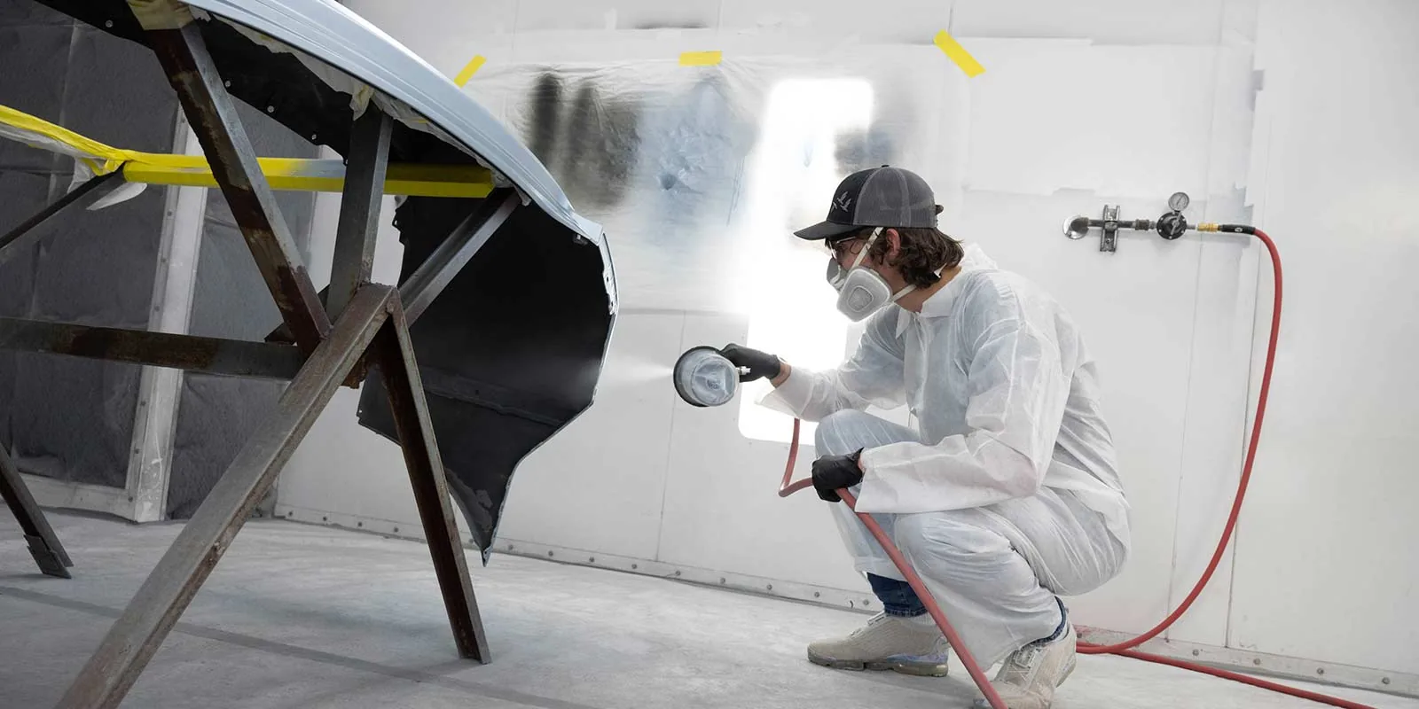 Panel beater spray painting a car bonnet during a colour-matched repair